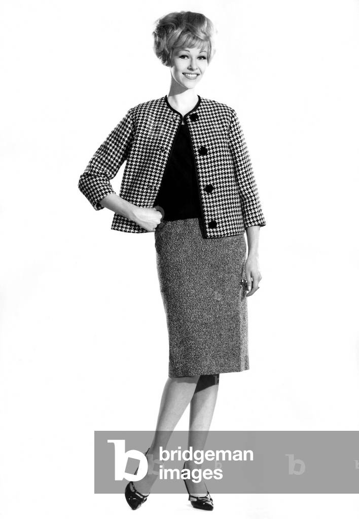 Model Jo Waring wearing skirt with jacket and top, standing with hands on hips. 
September 1962