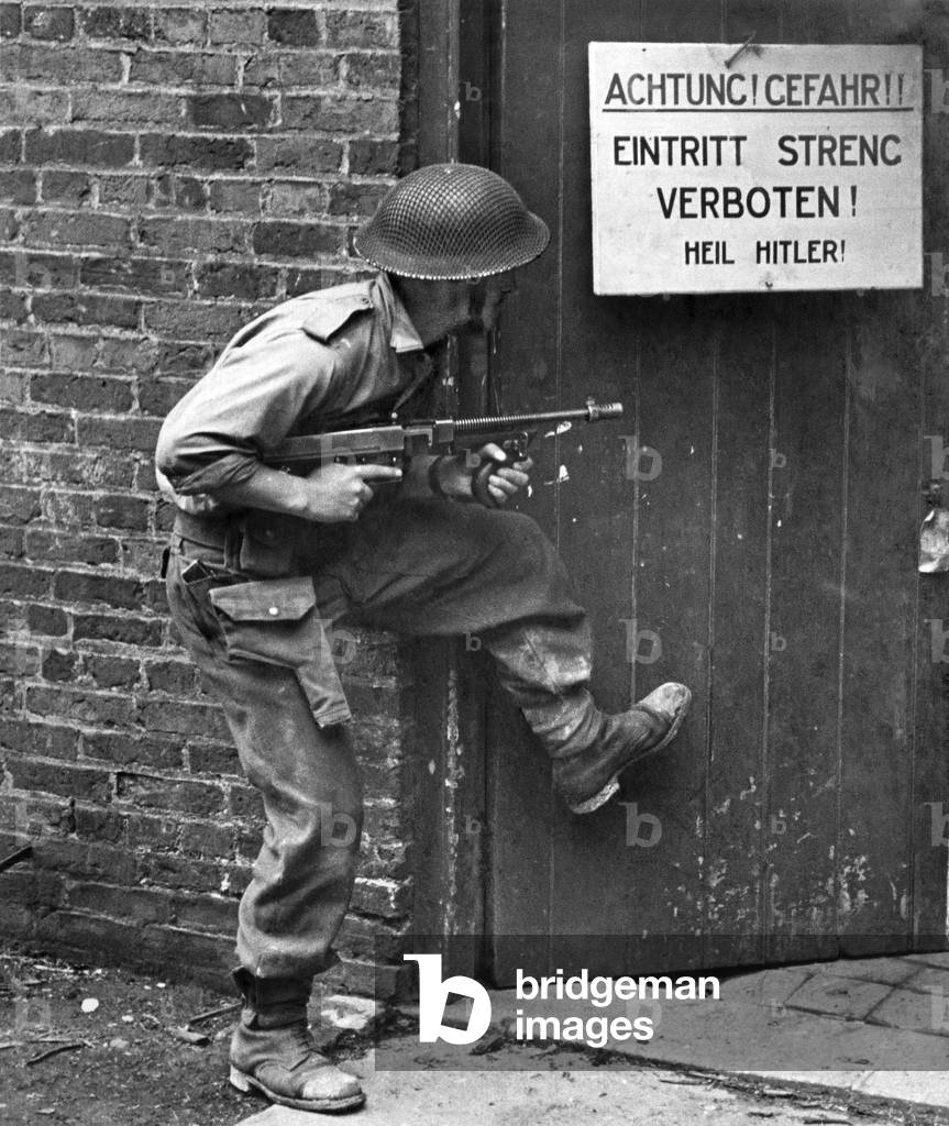 British Army Soldier uses a tommy gun while training to storm a mockup German building May 1942 (b/w photo)