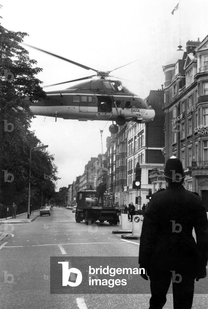 Good Morning Officer, Won't Be A Minute: A policeman keeps a careful watch as a helicopter hovers low over London's Belgravia. The helicopter dropped in to hoist three giant generators on to the roof of the Carlton Towers Hotel. With a mammoth crane the operation would have taken three days and caused chaotic traffic jams. The airlift on Sunday morning (30-9-73) took just twelve minutes and no one got a parking ticket. October 1973