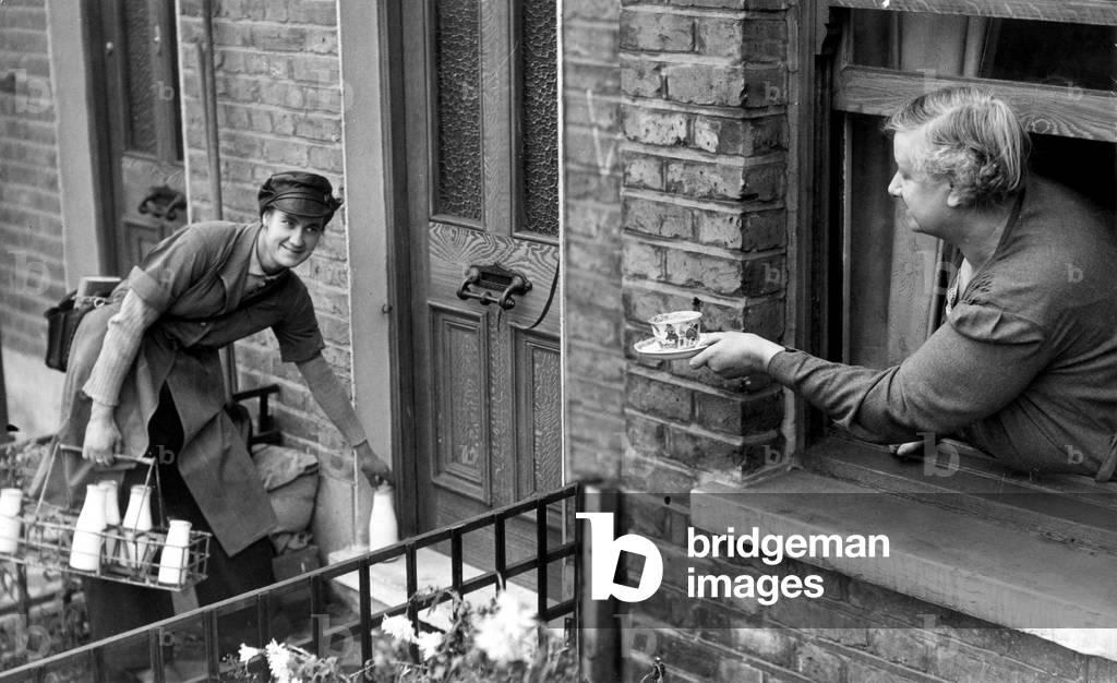 May Pearce, a milk girl, being given a cup of tea by her mother, 29th November 1942 (b/w photo)