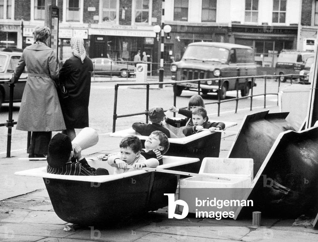 Boat race fever hits West London. Children from the Harwood Primary School act out the boat race in bath tubs outside a builders merchants in The Kings Road, 26th March 1971 (b/w photo)