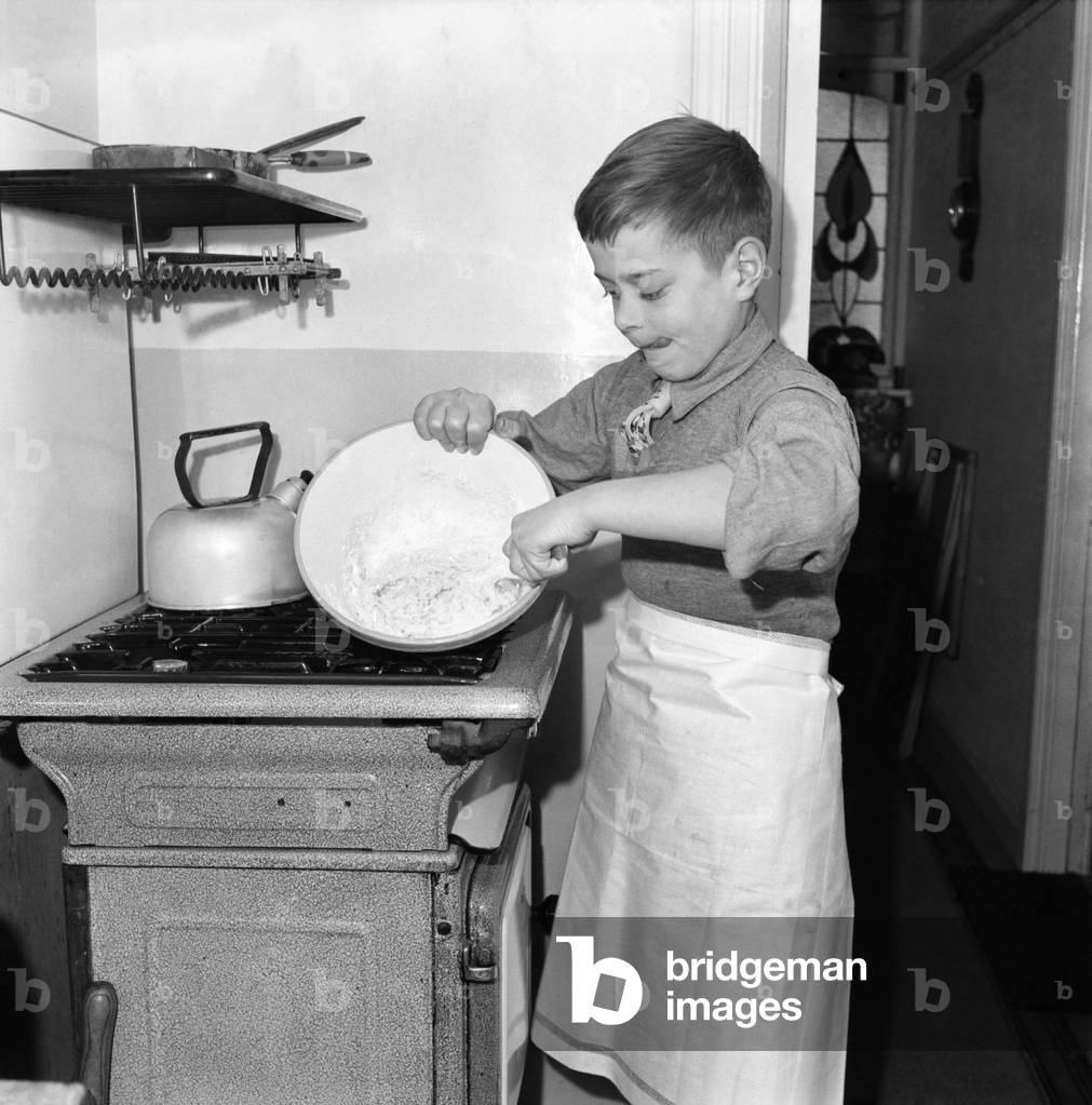 A young mixing ingredients together in a bowl in his kitchen at home. December 1952 C6055