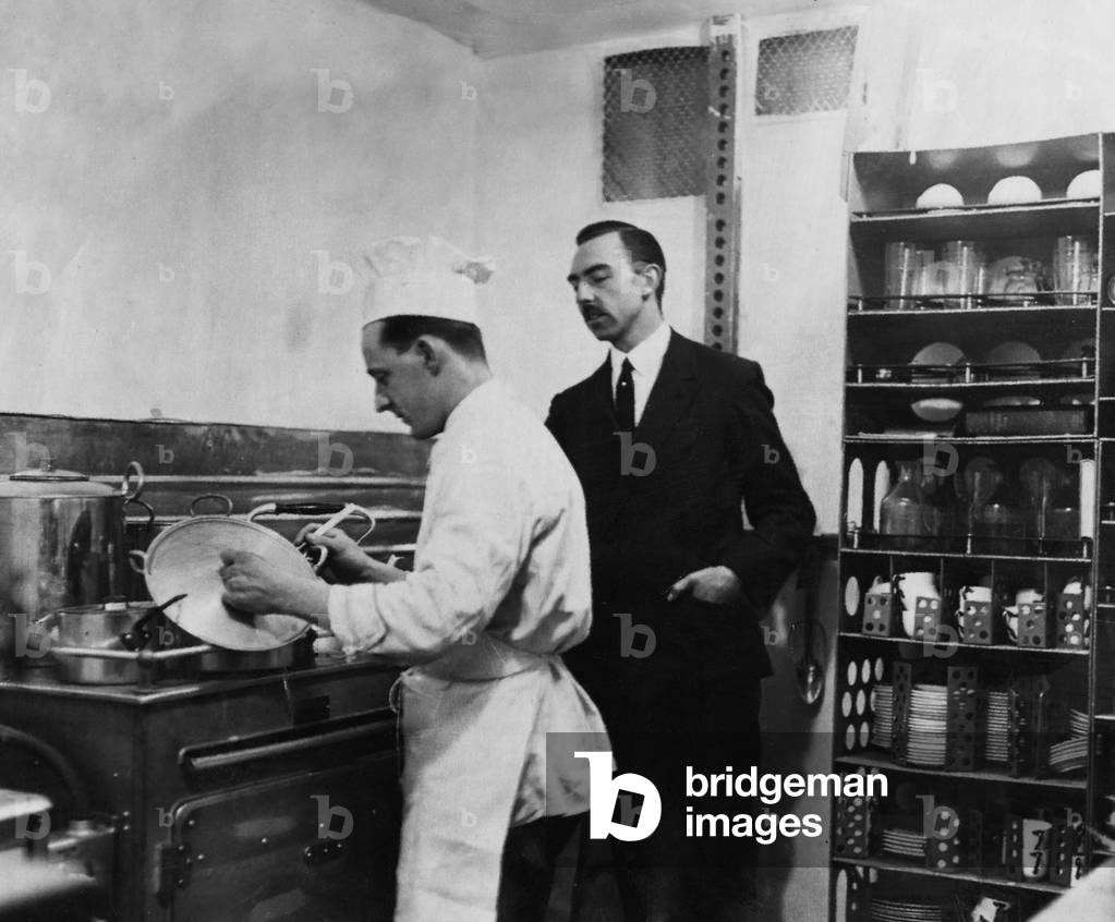 Eric Anderson Graham cook aboard the R101 seen here preparing a meal for the crew and passengers during one of the 1930 proving flights whilst Chief Steward Albert Savidge looks on, c. January 1930 (b/w photo)