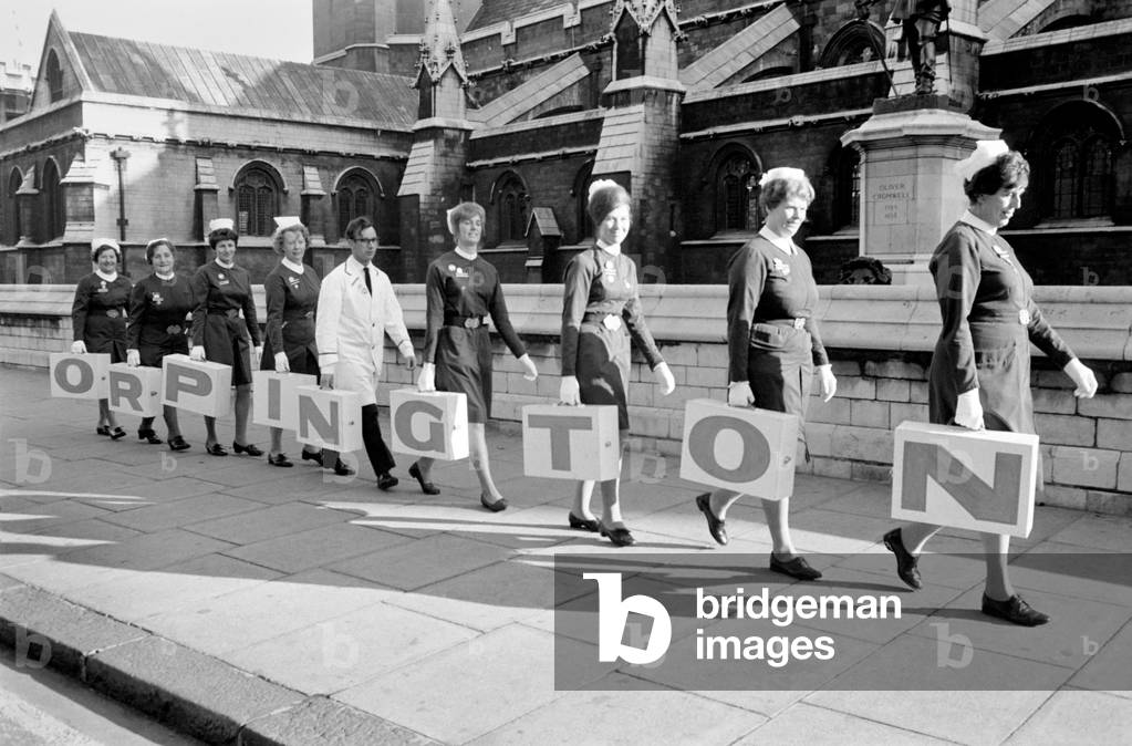 Uniformed nurses from Orpington Hospital went to the House of Commons today to hand over a petition to parliament to Mr. Eric Lubbock, MP for Orpington. Nine nurses carried from 30,000 petition signatures in large white boxes each painted with the letter from the word 'Orpington' and on the reverse side each box bore a red cross. The nurses were accompanied by several Citizen Members of the Orpington Nurses and Citizens Association. Although the petition refers specifically to Orpington Hospital, it is known that a shortage of nurses is affecting many hospitals in Britain. The nurses were not agitating for more pay and less working hours, but they were calling specifically for increased nursing establishment - in other words authority to recruit more nurses. The line-up of nurses with their white boxes containing the signatures, spelling the word Orpington, on their way to the House of Commons. November 1969