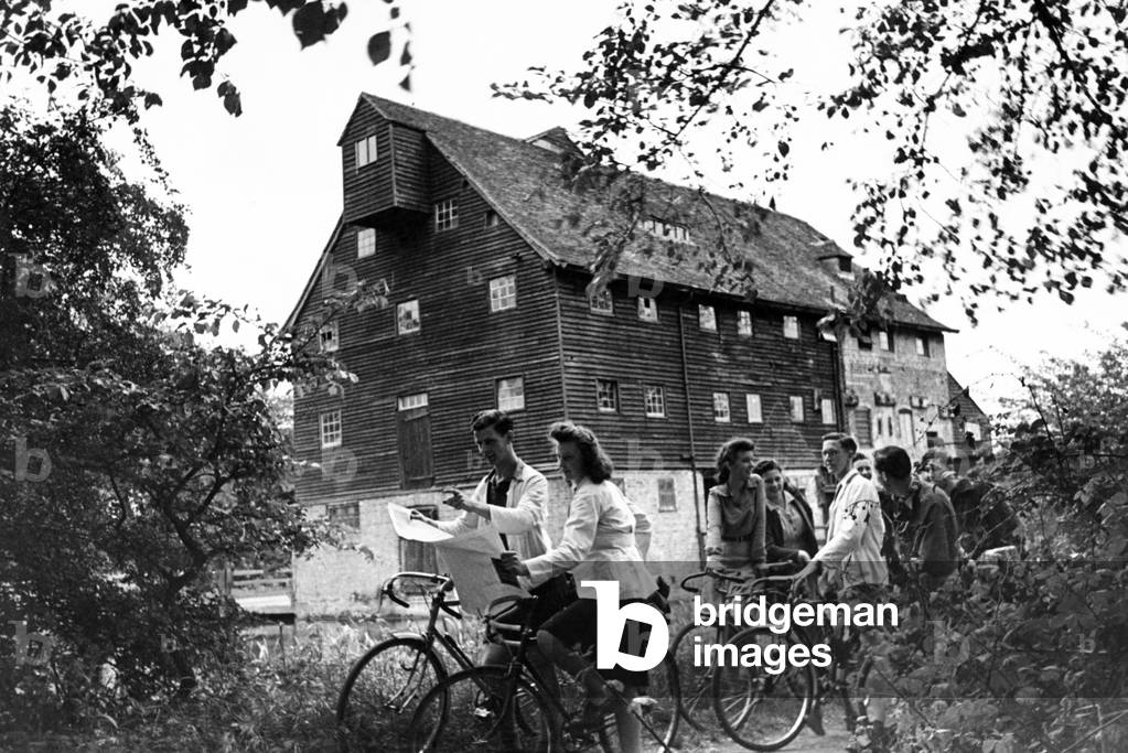 The Youth Hostel Association has fitted the 16th Century Elizabethan Houghton Mill on the River Ouse, near St Ives, Cambridgeshire, to accommodate 56 hostellers. They pay 1/- a night and sleep where the graet stones once ground the corn. Part of the mill is fitted as a cookhouse and the hikers bring along sausages and other provisions and cook for themselves. May 1945. (b/w photo)
