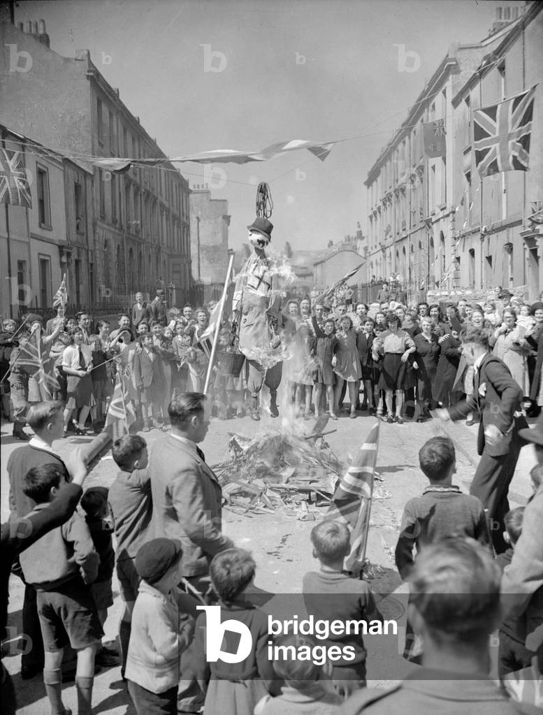 At 3pm on 8 May 1945, Prime Minister, Winston Churchill announced that the war in Europe would end at midnight. London erupted into a massive chorus of jubilation and celebration. Mr Churchill was greeted by huge cheering crowds wherever he went and the King was kept busy by a crowd outside Buckingham Palace who made him keep returning to the balcony to receive their accolades. Even his own daughters, escorted by Palace guards, joined the crowd in shouting for the King. All licensing laws in the capital were revoked for the evening and the celebrations went on well into the small hours. Our Picture Shows: Effigy of Hitler is burny in a South London street following the announcement of Victory in Europe following the surrender of Germany May 1945 (b/w photo)