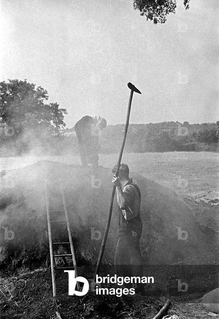 Two men burning peat in a field on a farm in England, c. 1938 (b/w photo)