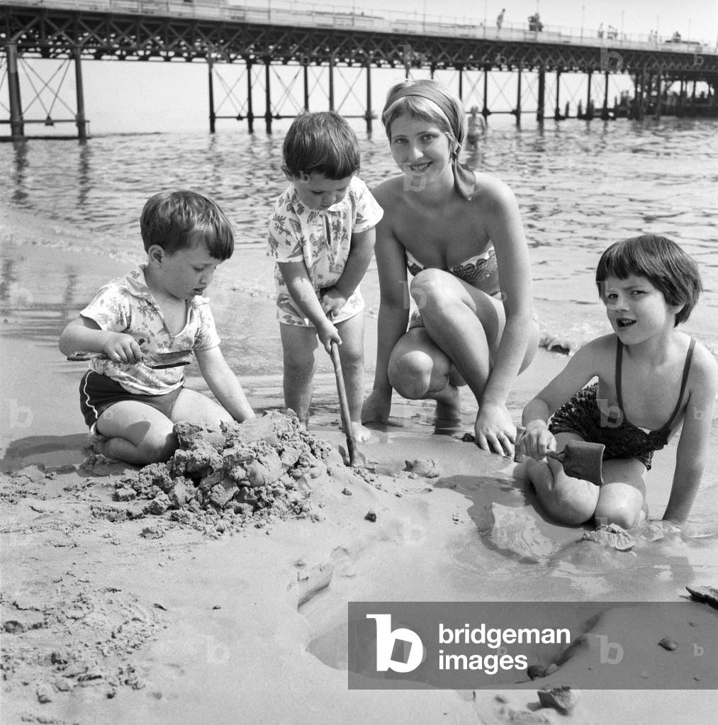 19 year old nanny Birte Anderson on the beach at Bournemouth with children Elizabeth (6), Kenneth (3), Nina (2). 
June 1960