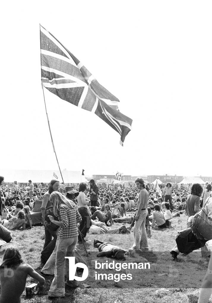 Reading Pop Festival. Young festival goers carrying the Union Jack flag as they make their way to the main stage, 24th August 1973 (b/w photo)