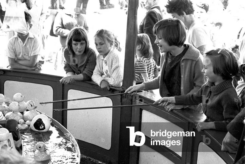 Children enjoying a game of 'Hook-a-Duck' at a stall.
Hearsall Common fair, Coventry.
3rd June 1963