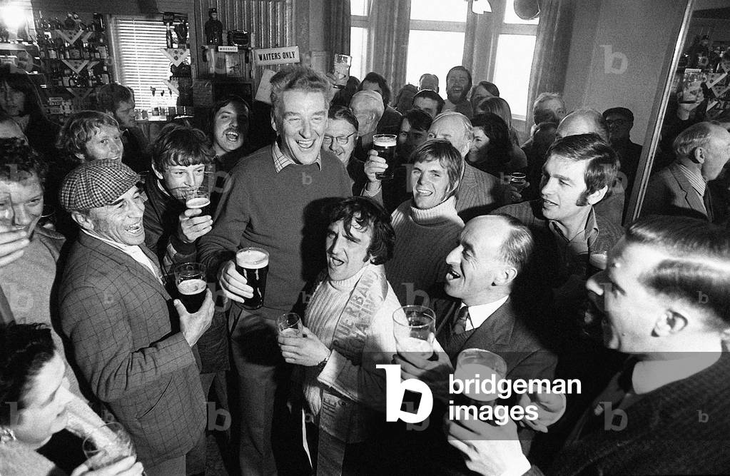 Donald Ginger McCain, trainer of Red Rum Racehorse, pictured drinking a pint of Guinness as he celebrates with stable lads in pub nearby stables after winning the Grand National. 31st March 1973 (b/w photo)