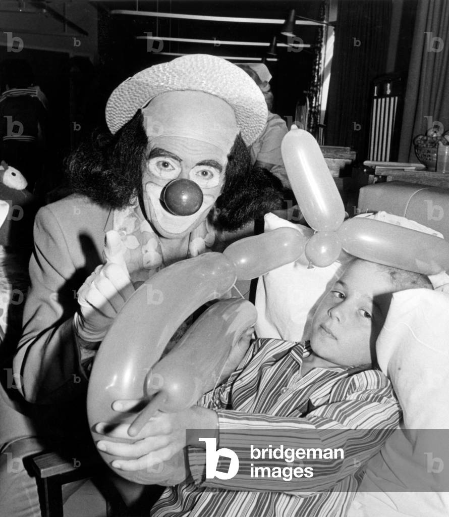 The clown Windy Blow visiting Middlesbrough Hospital, seen with a child holding a balloon sculpture. 2nd August 1979 (b/w photo)
