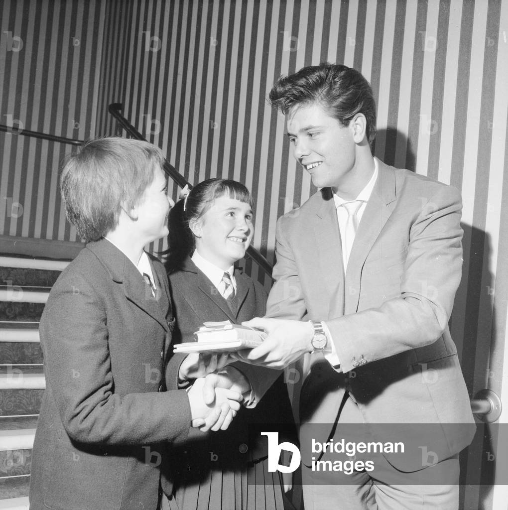 Singer Cliff Richard seen here presenting a school prize of three books to Carol Chamberlin at the Hugh Myddelton School as her friend Jean Arbuckle looks on. October 6th 1960 (b/w photo)