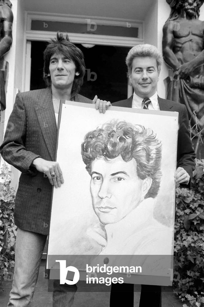 Rolling Stones: Ronnie Wood holds a painting of author Ken Follett who stands next to him. September 1987