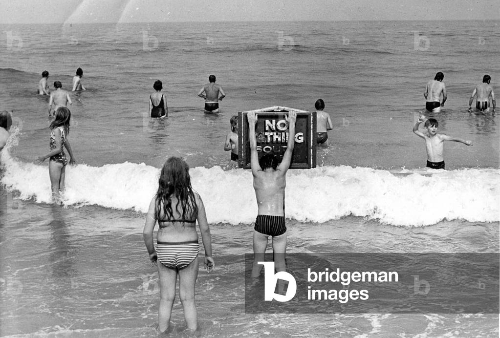 Holidaymakers risk their lives by ignoring the NO BATHING signs at this North East beach, 6 August 1975 (b/w photo)