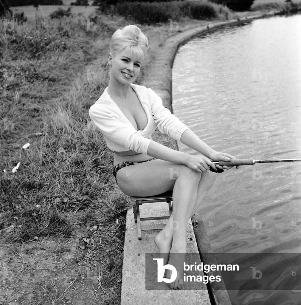Beachwear model by the river bank fishing, August 1963 (b/w photo)