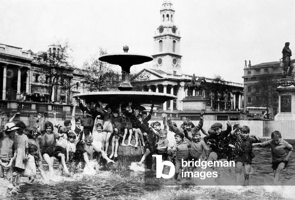 A crowd of children cool off in one of the fountains in Trafalgar Square during the Whitsun holiday St Martins in the Field Childhood Sitting on fountain Trousers rolled up Summer Cooling Off Paddling London May 1926 (b/w photo)