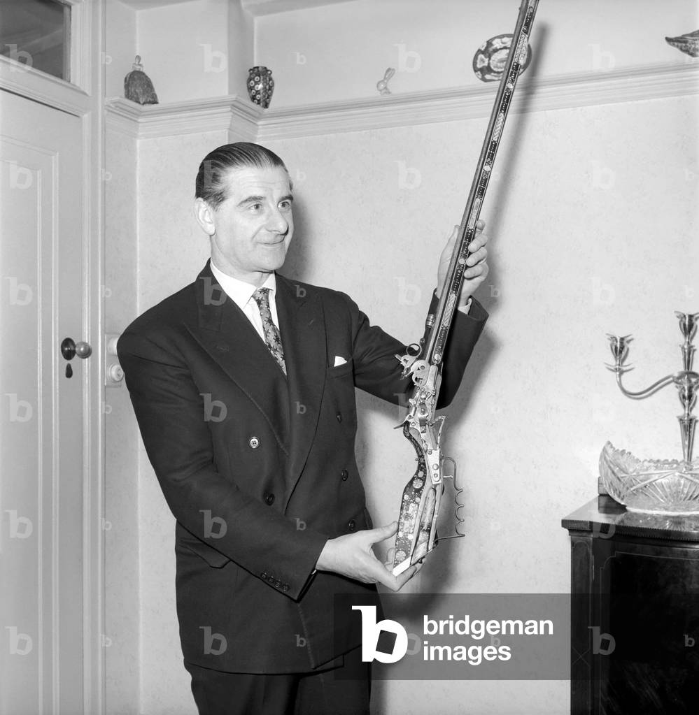 Pip Roberts a collector of antique firearms, seen here demonstrating a flintlock rifle, c. 1957 (b/w photo)