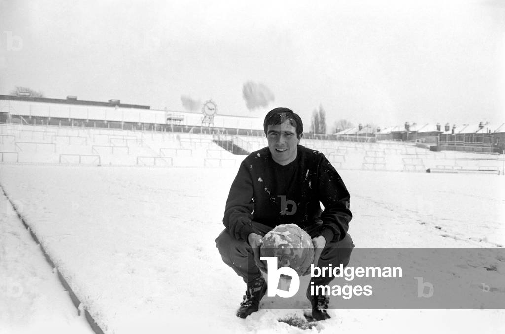 Arsenal's transfer lister forward, Bobby Gould, who was to have played for Arsenal reserves and West Ham reserves at Highbury, donned his track-suit and loosened up on the pitch for our cameraman, in very thick snow in front of a completely deserted stadium. With only the famous Arsenal clock visible, Bobby Gould still smiles in frozen Highbury Stadium. November 1969 (photo)