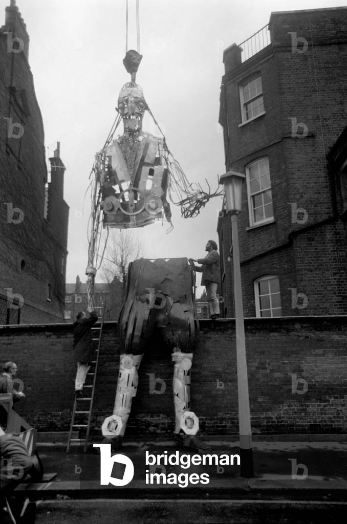 Gulliver, all 21ft of him, weighing 6cwt, made of metal, needed a crane to start him on his journey from Cheyney Walk in Chelsea to Tokyo, Japan. Gulliver is the metal creation by cartoonist, artist, Gerald Scarfe and is one of twelve characters that Gerald is making for the British Pavilion at the Expo '70 to be held in Tokyo in March. The metal monster took Gerald three months to put together, using welding apparatus, he made is in the garden of his home in Chelsea in two halves and each half had to be hoisted by crane from the garden, over two garden walls to the side road where it was packed away into large crates. The other characters that Mr. Scarfe will be working on are Hamlet, MacBeth, Robinson Crusoe, Samuel Johnson, Long John Silver, Pick Wick, Alice 'thru the looking glass, Oliver, Shakespeare, James Bond and My Fair Lady. Bearded Gerald Scarfe with Gulliver. December 1969