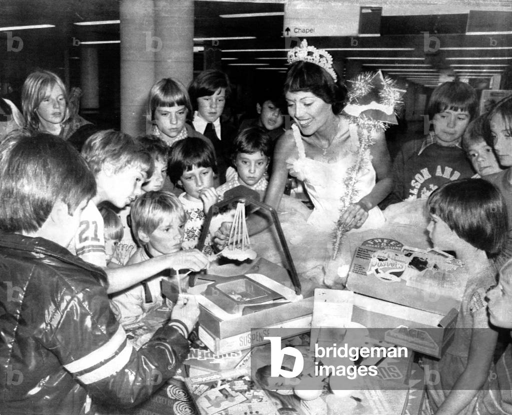 A glittering fairy queen dropped into Gatwick Airport and cheered many holidaymakers grounded by the air traffic controllers' dispute. Children made a bee-line to the fairy, model Susie Hart, who proceeded to hand out piles of toys, games and craft sets from her 'carriage' a luggage trolley. In fact, the goodwill gesture gifts were from the newly-formed Wiggins Teape Toys and Crafts Company, based ar Brentwood, Essex and although the idea had a publicity thought behind it, everyone concerned agreed it was a nice idea to relieve the tension. 25/08/1977 (b/w photo)