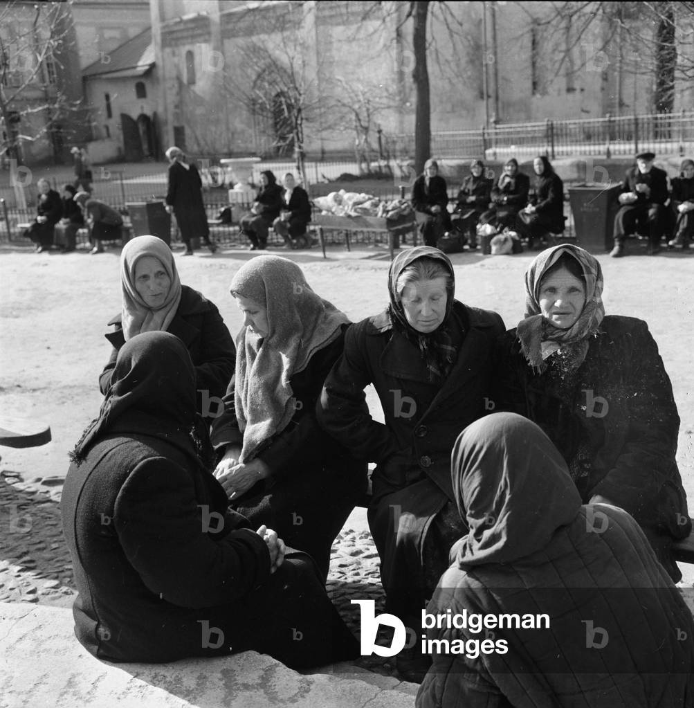 Female residents of the Soviet town of Zagorsk sitting together talking as they gather in front of one of the churches in the town. 
May 1960