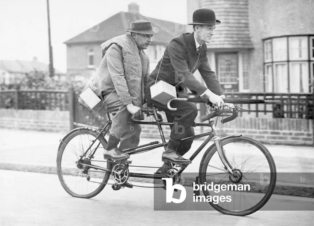 Two business men who usually travel to town by car share a tandem cycle after the introduction of petrol rationing on the 22nd September 1939 (b/w photo)