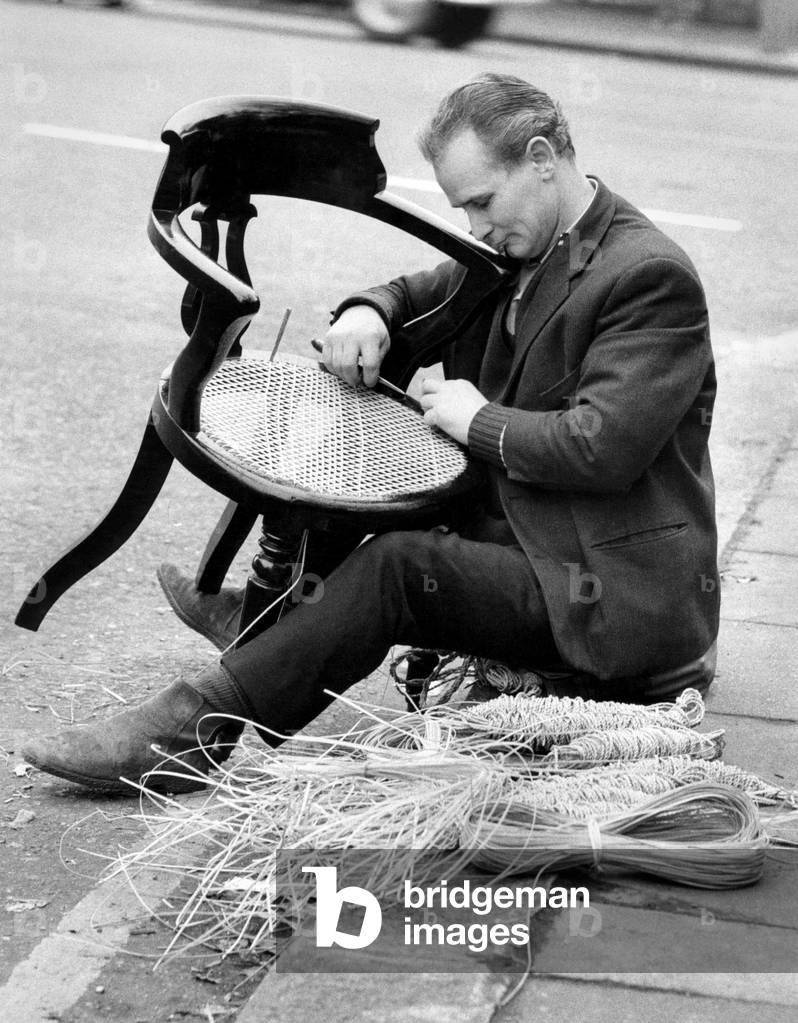 Chair Caning: An unusual sight in London the old craft of chair caning Mr. John Browning 38 year old from Battersea, repairing a cane chair, sitting on the edge of the pavement, on the corner of Ladbroke Grove. He learnt the craft from his 65 year old father-in-law who has been doing it all his life. He travels around London and gets work on recommendation. January 1971