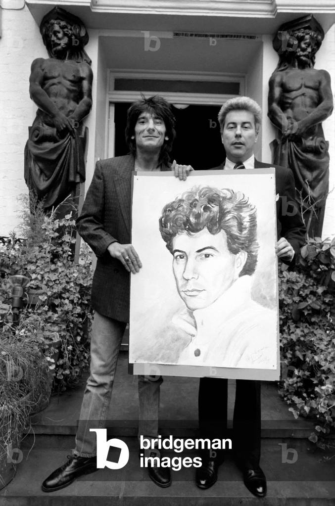 Rolling Stones: Ronnie Wood holds a painting of author Ken Follett who stands next to him. September 1987
