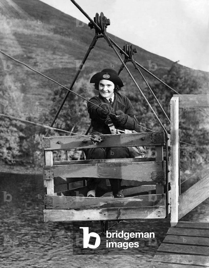 World War II Women. Pulling her weight. Miss Joan Niven, 19 year old postwoman of Drynachan, near Inverness, Scotland claims to have the most isolated beat in the British Isles. She walks 17 miles three times in a week, to cross the River Findhorn she uses a box suspended on a wire cable pulling herself over by another wire. Seven persons are seen by her during the walk of 17 miles. Last winter ice and snow on the moor tracks prevented the small motor mail van from contacting Miss Niven, she walked seven miles through the snow to meet the van for several weeks. Miss Niven started this job to aid the war effort but she is thinking of joining the W.A.A.F's. Here Miss Joan Niven fording the River Findhorn. November 1941