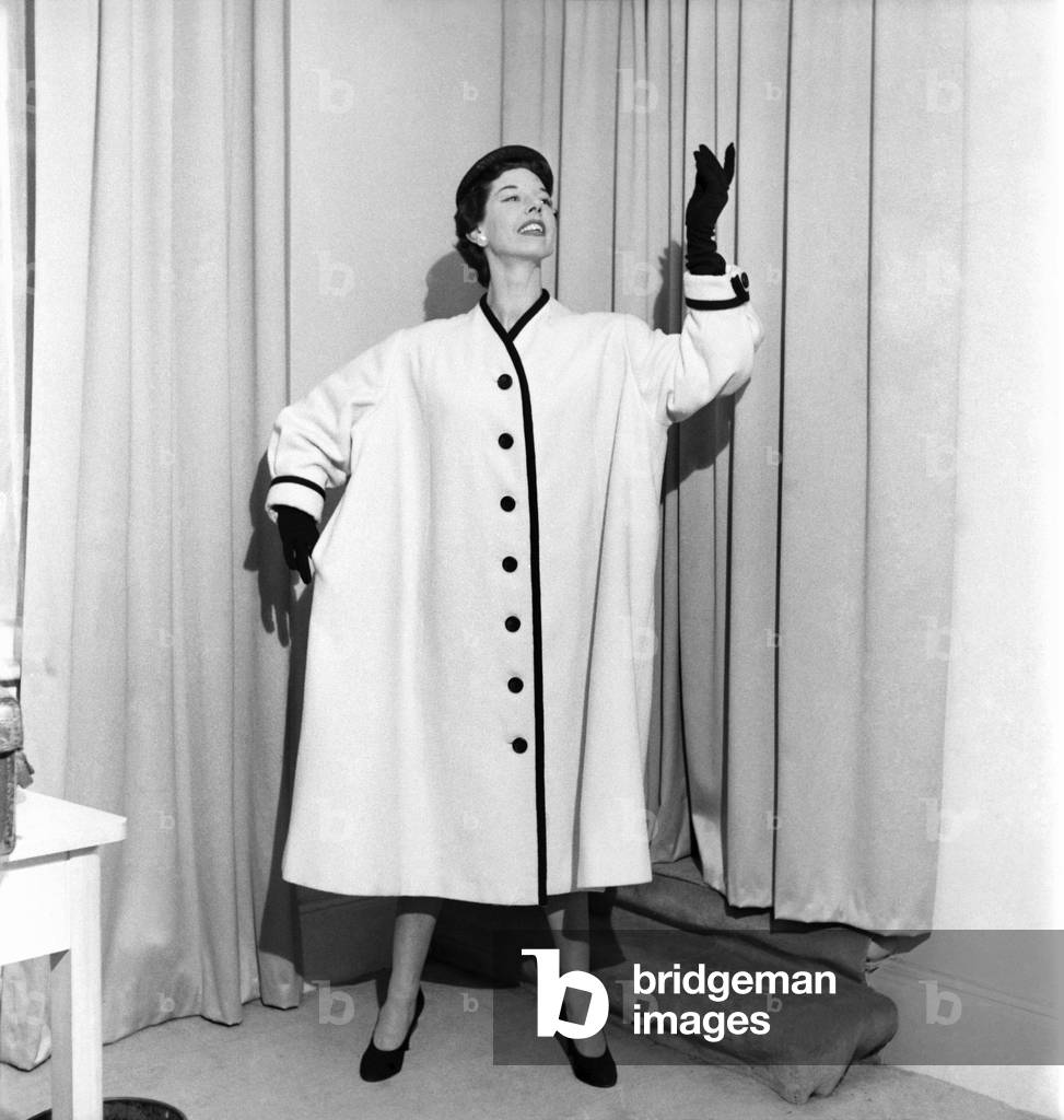 Clothing: Fashion. Model Dorothy Emms wears a white woollen coat with black trim. Note the extreme fullness. This coat is called 