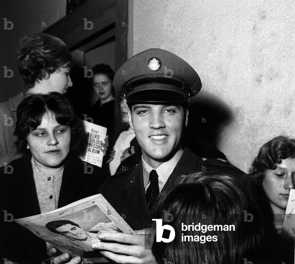 Elvis Presley signs autographs at press conference for fans in Germany, March 1960 (b/w photo)