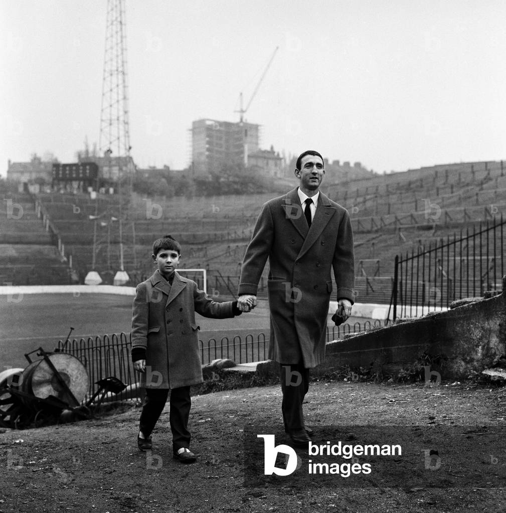 Former Charlton Athletic player Eddie Firmani who left England in 1955 to join Italian team Sampdoria is pictured on his return to England for a few days holiday. He is staying at the home of his in laws in Catford, South London. Here he is photographed with his son Paul at his former club's ground The Valley. 8th November 1962 (photo)