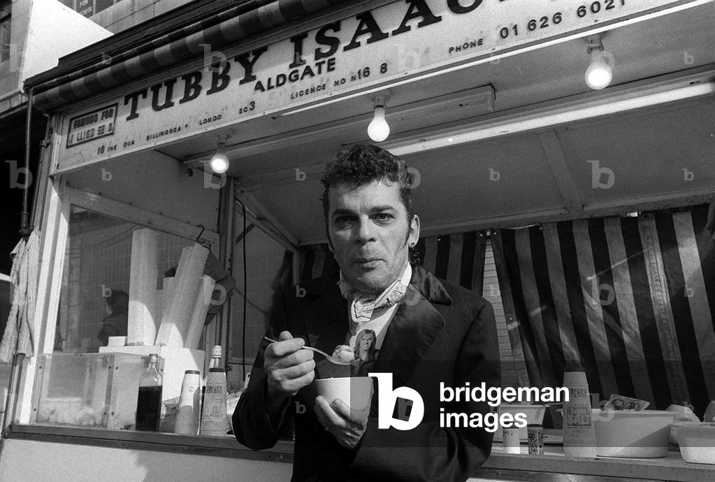 Ian Dury outside the East End stall of Tubby Isaacs eating bowl of Jellied eels. 1978