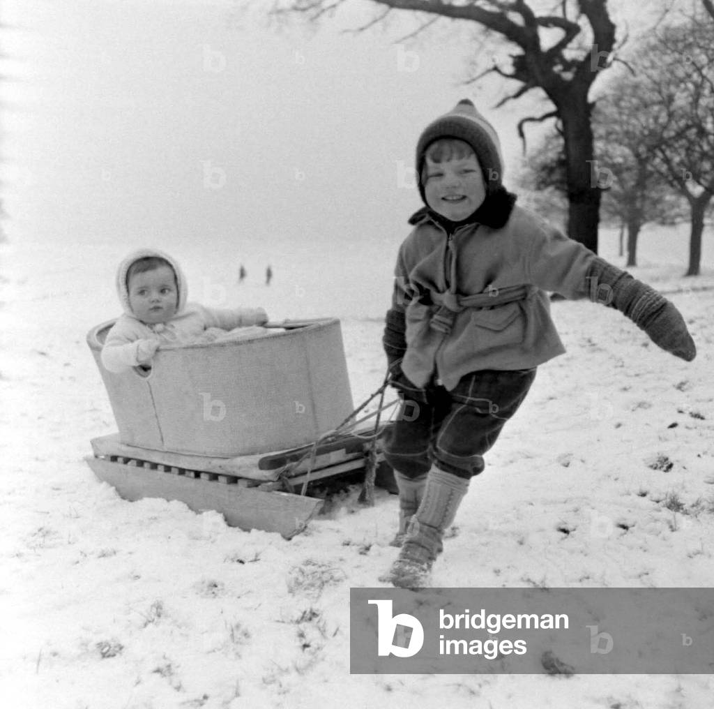 Three year old girl Linda Torkington pulls along her 10 month old baby sister Susan in a sledge on the snow clad slopes of Lyme Park in Cheshire after a heavy snowfall, 20 January 1960 (b/w photo)