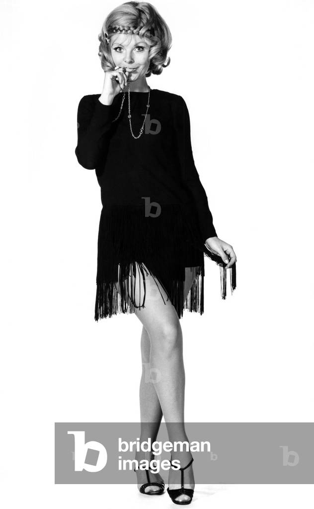 Jazzy. Charleston girl roars back to fashion in a flirty vamp dress. Cut short and swinging in black crepe, it has a two-tier fringe from the hipline. By Polly Peck, price £9 5s. November 1969