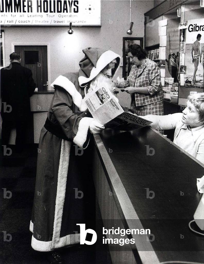 Father Christmas in a travel agency booking his summer holiday, 23/12/1969 (b/w photo)