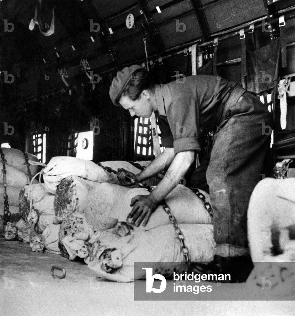 Coal supplies for the British, American and French sectors of Berlin are being flown in by the RAF from Fassberg near Celle in the British Zone of Germany during the Berlin Airlift. 
Driver Cox, R.A.S.C, tightens a chain securing service kitbags in a Dakota about to leave Fassberg for Berlin. 
July 1948