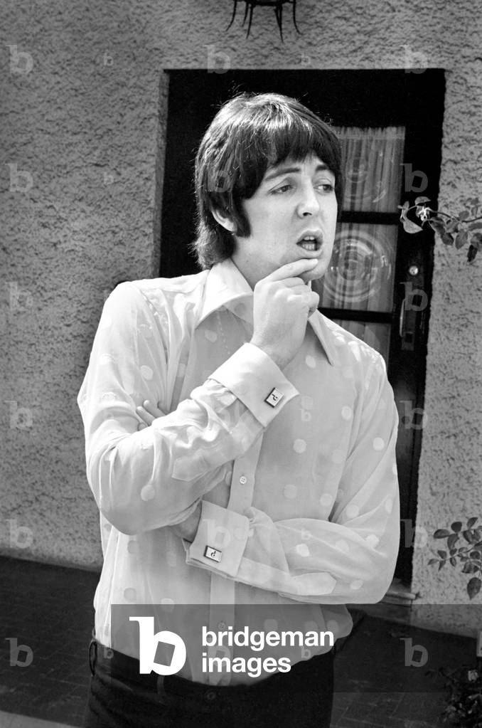 Beatles singer Paul McCartney relaxing in the grounds of his father's home in Gayton in the Wirral, Cheshire, wearing a pink polka-dot shirt and black slacks - and white plimsolls, July 1968 (b/w photo)