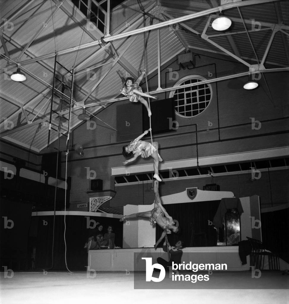 14 year old Johnny Pugh is the son of Digger Pugh who runs a troupe of 25 hire wire girls, all English, the act is to be in the circus at Harringay this year but just now Johnny his Dad and the girls have the use of Hownslow Swimming baths for practice till its time to move to Harringay Circus. 
When the girls practice up on the ropes he holds it steady just to stop any trouble. Note girls are from top to bottom: Syliva Wragg, Sheila Bush and Sheila McMahon. December 1952 C6171