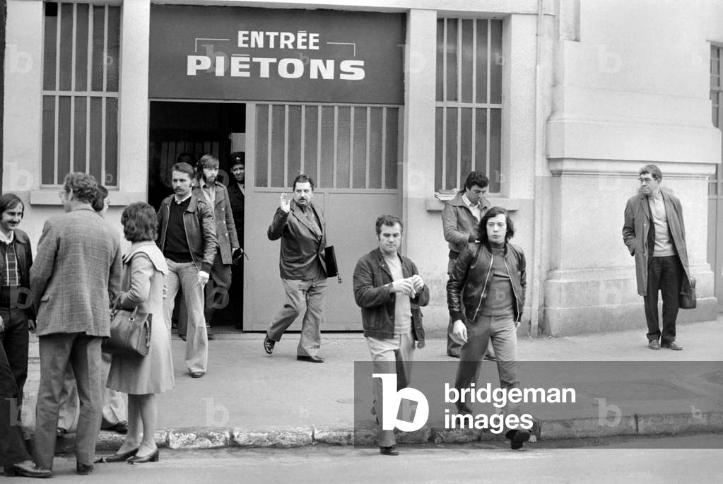 Renault factory workers leaving at the end of a shift through a door marked 'Pietons' in Paris, April 1975 (b/w photo)