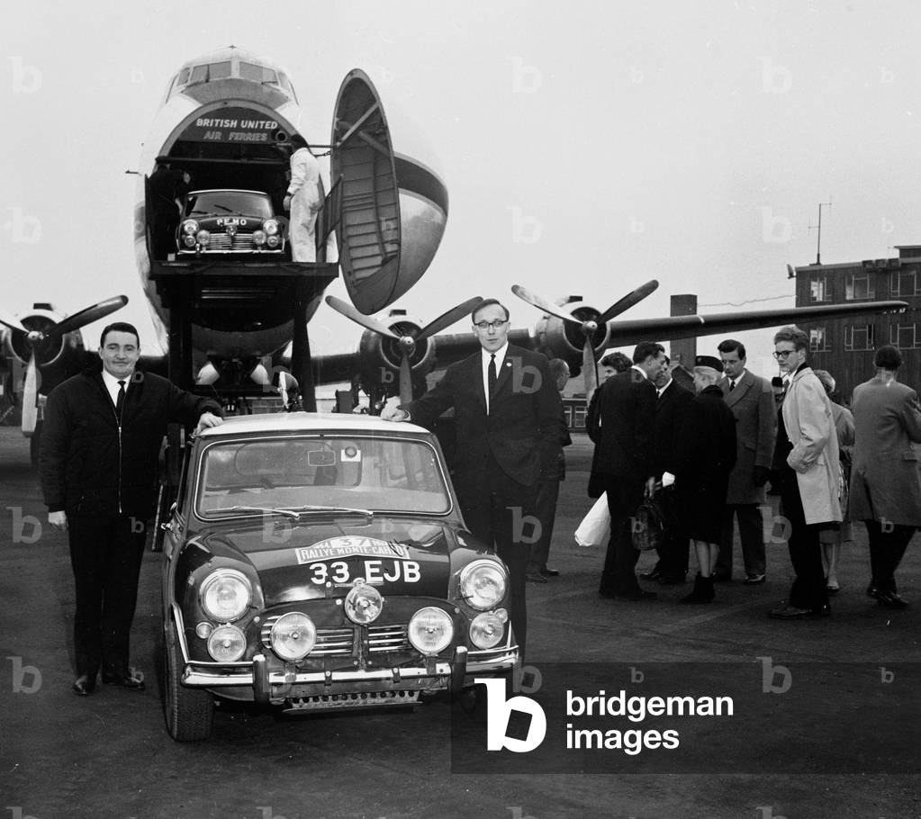 Paddy Hopkirk (l) and Henry Liddon arrive back in the UK after winning the 1964 Monte Carlo Rally in their Mini Cooper S. They are pictured standing beside their car at Southend Airport. 27th January 1964 (b/w photo)