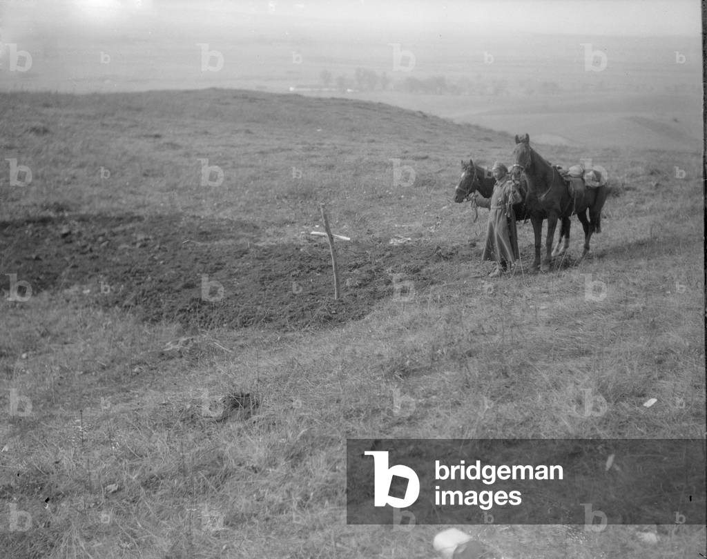 A lone Russian soldier stands by a mass grave in Galicia, September 1914 (b/w photo)