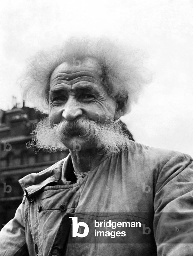 An eldelry man with with white fuzzy hair and matching beard, smiles for a portrait. 
Circa 1969