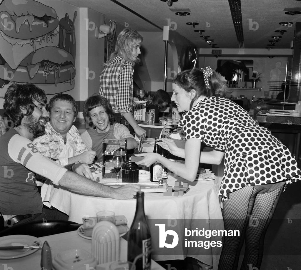 Games mistress Doni with customers and Mr Freedom owner Tommy Roberts (second left) trying out some of the new games. Mr Freedom's restaurant at 20 Kensington Church Street, London. The restaurant is in the basement of Mr Freedom clothing boutique. 30th July 1971 (b/w photo)