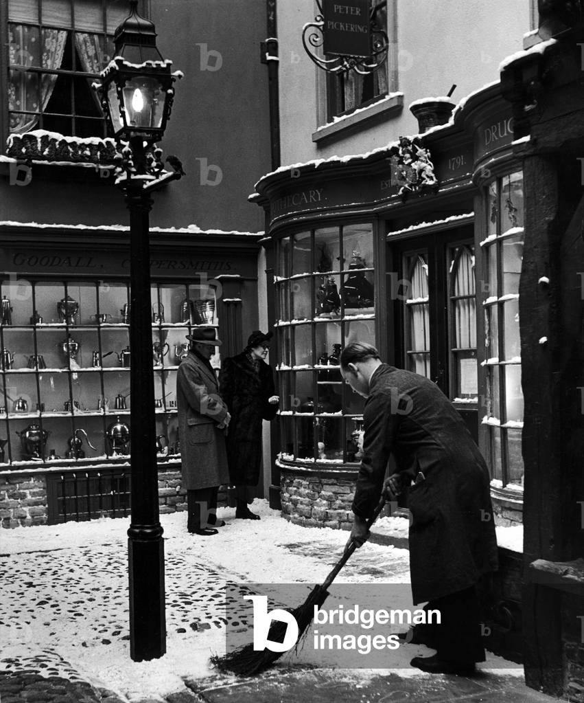 There is a cobbled street of Tudor and Victorian York shops in the Castle museum, York. The shops are named after well known York tradesmen, The snow has been laid to give a seasonable appearance. 2nd January 1952 (b/w photo)