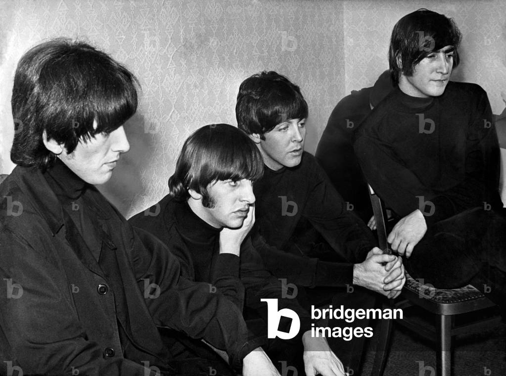 While the fans scream, the Beatles sit calmly backstage - watching themselves on television - before their appearance at the Odeon cinema, New Street, Birmingham. Left to right: George Harrison, Ringo Starr, Paul McCartney and John Lennon. 09/12/1965 (b/w photo)