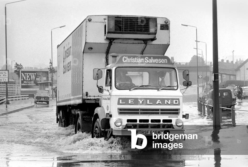 Floods in North London following a rainstorm that dumped over two inches of rain over southern England in a 12 hour period. Our Picture Shows: A lorry make its way through a flooded Harrow Road, August 1977 (b/w photo)