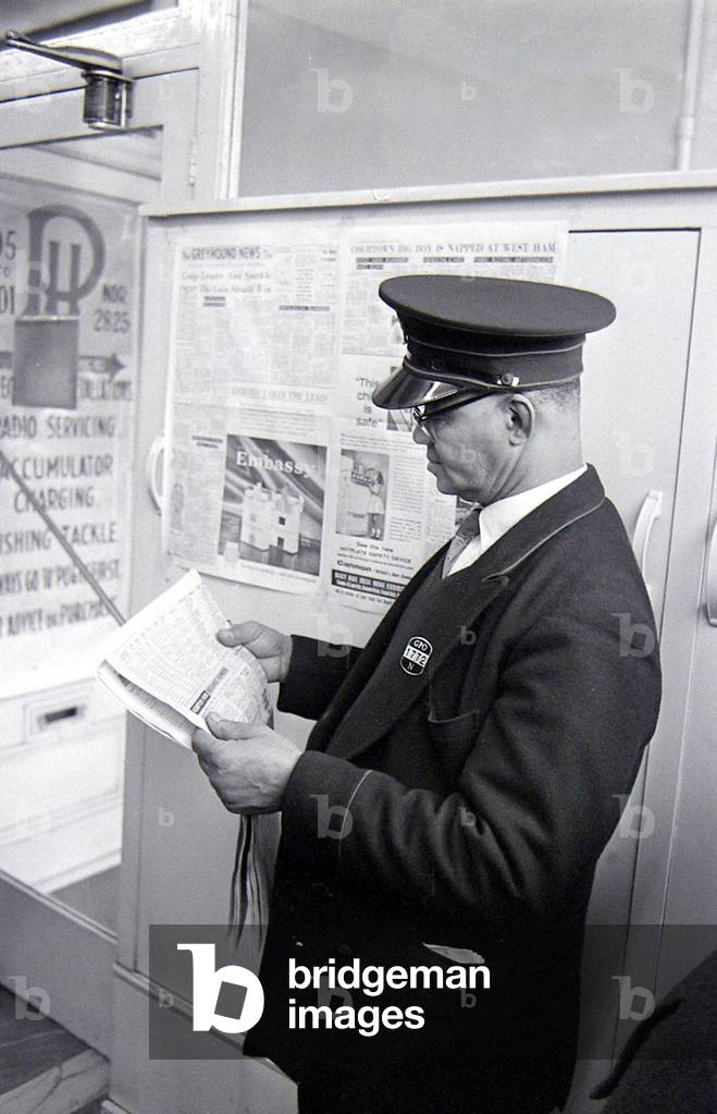 A security guard checking the racing guide in a newspaper, March 1963 (b/w photo)