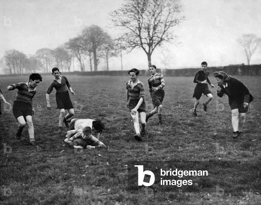 While the sports master is away fighting at the front the sports mistress who usually referee's the girls hockey match takes over refereeing duties of the boys rugby match November 1943